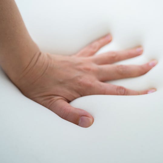 A hand touching a memory foam mattress
